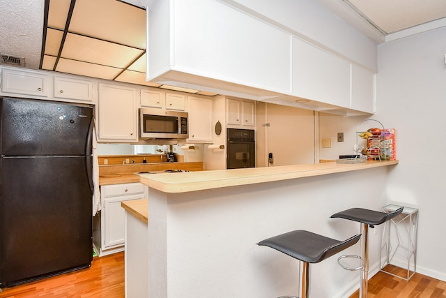 kitchen with a breakfast bar, white cabinetry, black appliances, kitchen peninsula, and light wood-type flooring