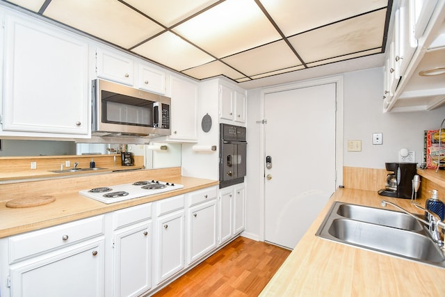 kitchen with sink, black oven, white stovetop, white cabinetry, and light wood-type flooring