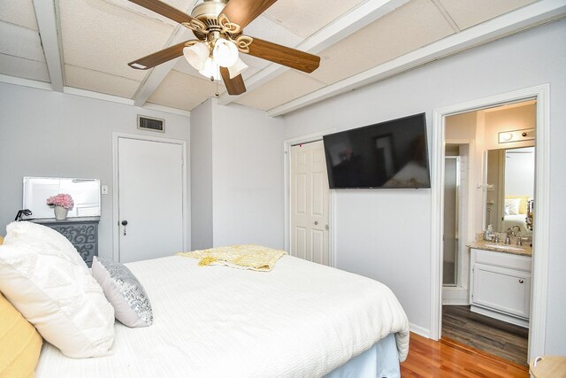 bedroom featuring beamed ceiling, wood-type flooring, sink, ceiling fan, and a closet