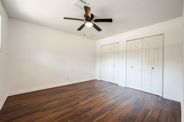 unfurnished bedroom featuring ceiling fan, dark hardwood / wood-style flooring, and two closets