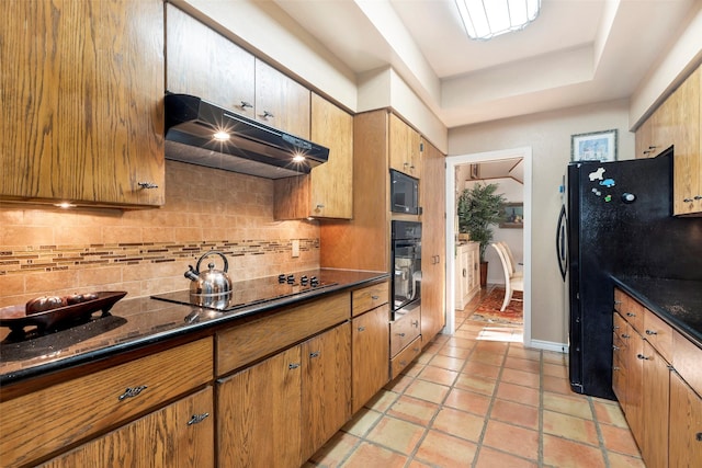 kitchen featuring tasteful backsplash, light tile patterned floors, a raised ceiling, dark stone counters, and black appliances