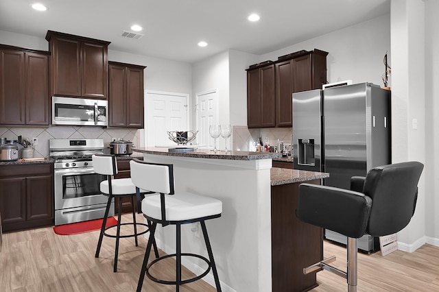 kitchen with light wood-type flooring, dark stone countertops, a kitchen breakfast bar, a kitchen island, and stainless steel appliances