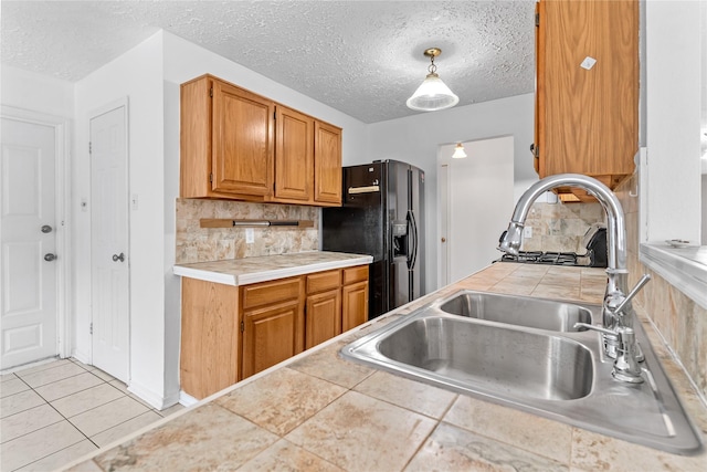 kitchen with sink, backsplash, black fridge with ice dispenser, tile countertops, and decorative light fixtures