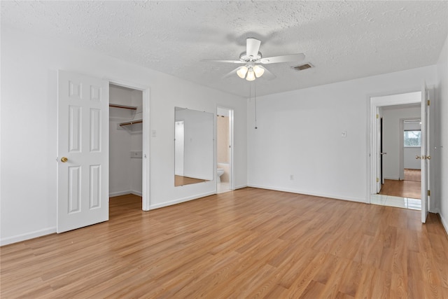 unfurnished bedroom featuring a walk in closet, a textured ceiling, a closet, ceiling fan, and light hardwood / wood-style floors