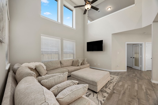 living room featuring ceiling fan, light hardwood / wood-style floors, and a towering ceiling