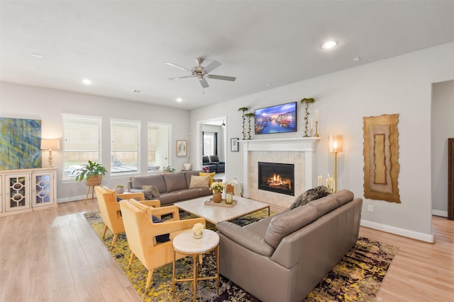 living room with a tiled fireplace, ceiling fan, and light hardwood / wood-style flooring