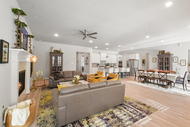 living room with ceiling fan, a tiled fireplace, and light hardwood / wood-style floors