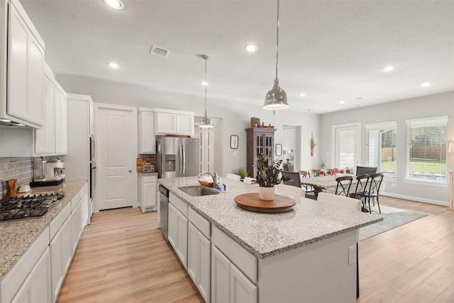 kitchen with a center island with sink, sink, pendant lighting, stainless steel appliances, and white cabinets