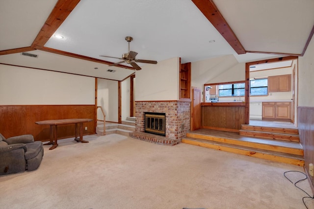 carpeted living room featuring ceiling fan, wooden walls, a fireplace, and vaulted ceiling with beams