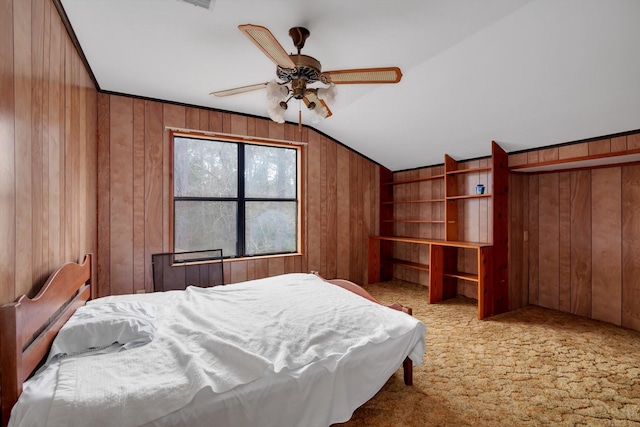 bedroom with vaulted ceiling, light colored carpet, ceiling fan, and wood walls