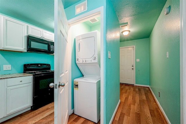 clothes washing area featuring stacked washer / drying machine, a textured ceiling, and light wood-type flooring