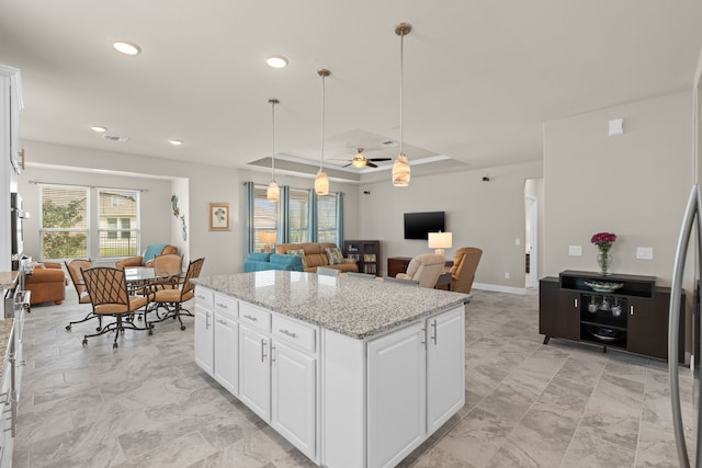 kitchen with light stone countertops, pendant lighting, white cabinets, and a tray ceiling