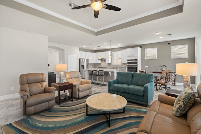 living room featuring ceiling fan, ornamental molding, a tray ceiling, and sink