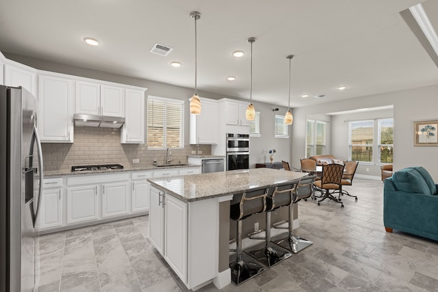 kitchen featuring hanging light fixtures, stainless steel appliances, light stone counters, white cabinets, and a kitchen island