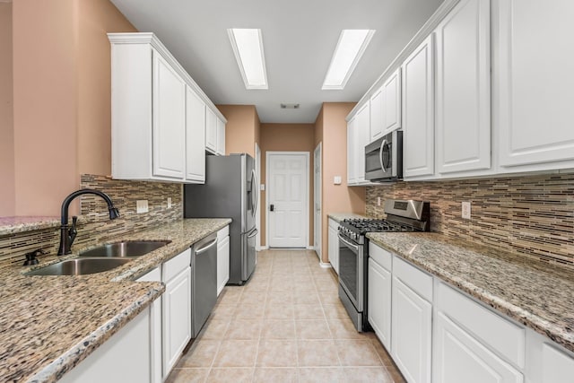 kitchen featuring sink, white cabinetry, light stone counters, light tile patterned floors, and appliances with stainless steel finishes