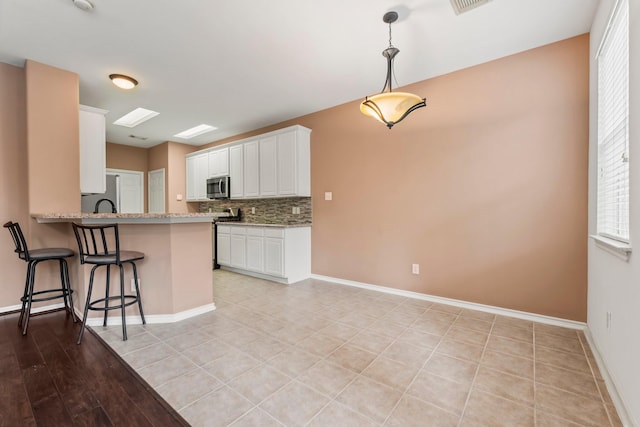 kitchen with tasteful backsplash, a kitchen breakfast bar, kitchen peninsula, pendant lighting, and white cabinets