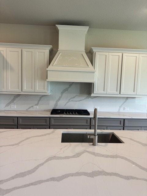 16147 Rustling Woods Rd, Conroe, TX 77302 - kitchen with custom range hood, a sink, decorative backsplash, black gas cooktop, and light stone countertops