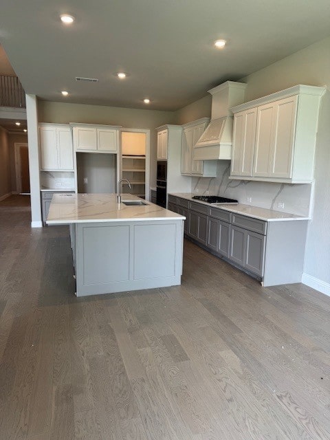 16147 Rustling Woods Rd, Conroe, TX 77302 - kitchen with custom range hood, a sink, wood finished floors, baseboards, and a center island with sink