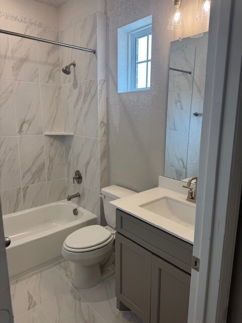 16147 Rustling Woods Rd, Conroe, TX 77302 - bathroom with a textured wall, bathtub / shower combination, toilet, vanity, and marble look tiles