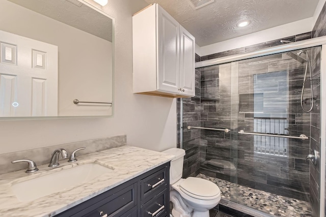 bathroom with a textured ceiling, toilet, vanity, and a shower with door