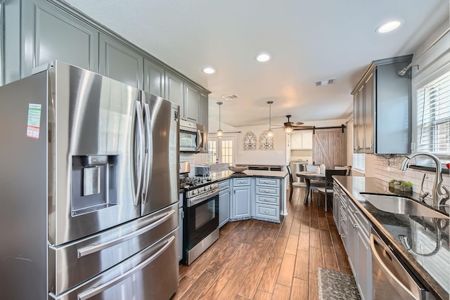 kitchen featuring hanging light fixtures, a barn door, sink, backsplash, and appliances with stainless steel finishes