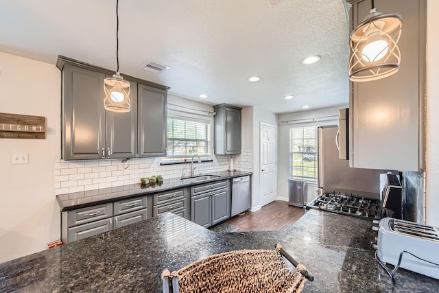 kitchen with gray cabinetry, hanging light fixtures, sink, dishwasher, and dark stone countertops