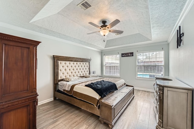 bedroom featuring crown molding, light hardwood / wood-style flooring, a tray ceiling, and a textured ceiling