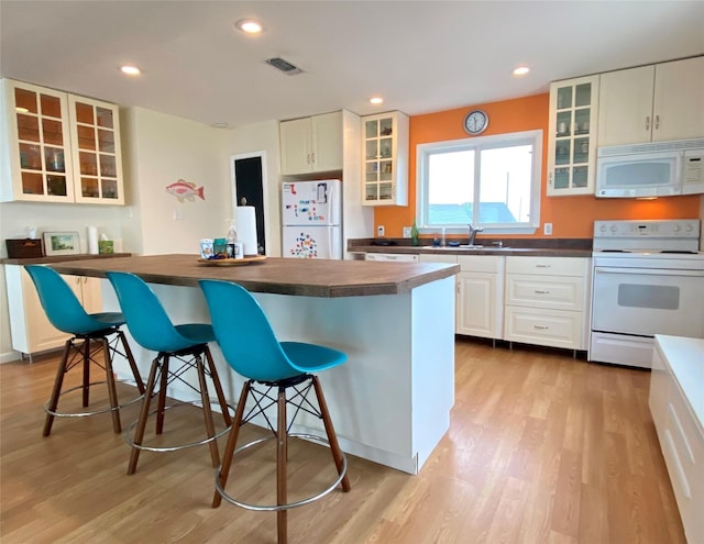 kitchen featuring sink, white appliances, a breakfast bar, and white cabinets