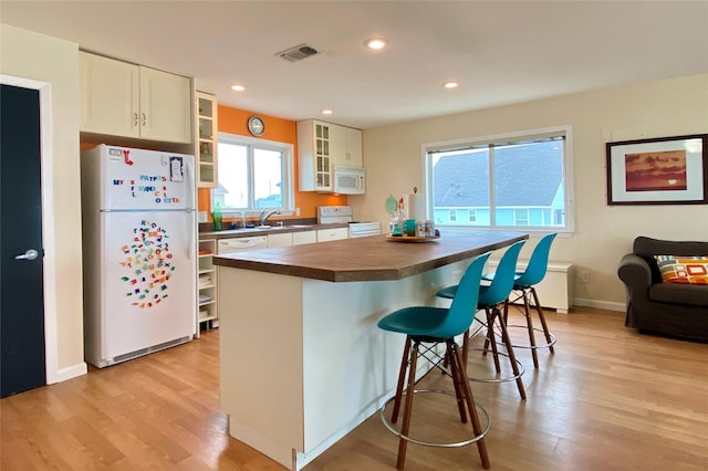 kitchen featuring white cabinetry, a center island, light hardwood / wood-style flooring, white appliances, and a breakfast bar area