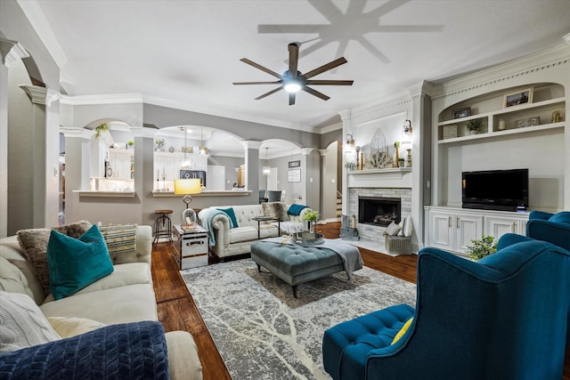 living room featuring ornamental molding, a fireplace, wood finished floors, and decorative columns