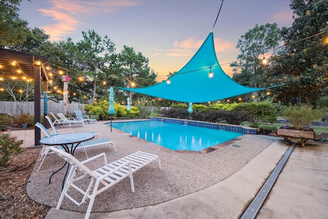 pool at dusk with an outdoor pool, a patio, and fence