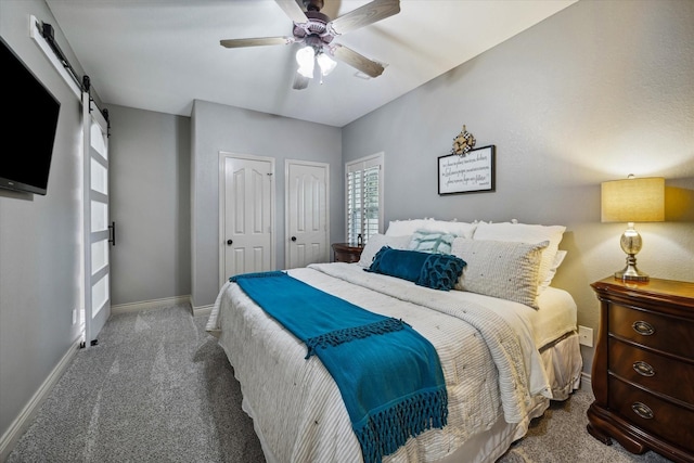 bedroom with carpet floors, multiple closets, a barn door, a ceiling fan, and baseboards