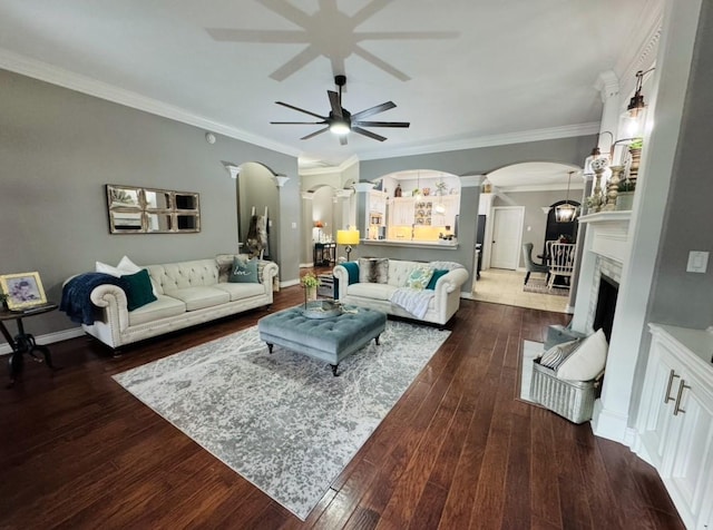 living room featuring dark wood-style floors, arched walkways, a fireplace, ornamental molding, and ornate columns