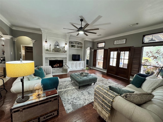 living room with a brick fireplace, visible vents, ornamental molding, wood finished floors, and ornate columns