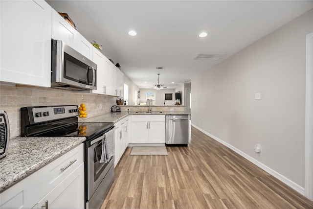 kitchen featuring white cabinetry, kitchen peninsula, stainless steel appliances, hanging light fixtures, and sink