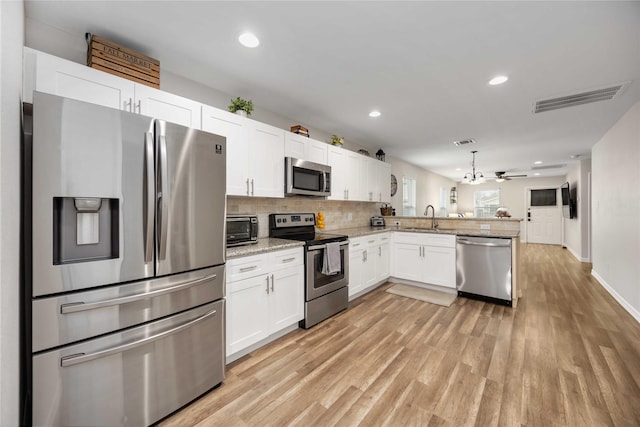 kitchen with appliances with stainless steel finishes, white cabinets, light hardwood / wood-style floors, sink, and kitchen peninsula