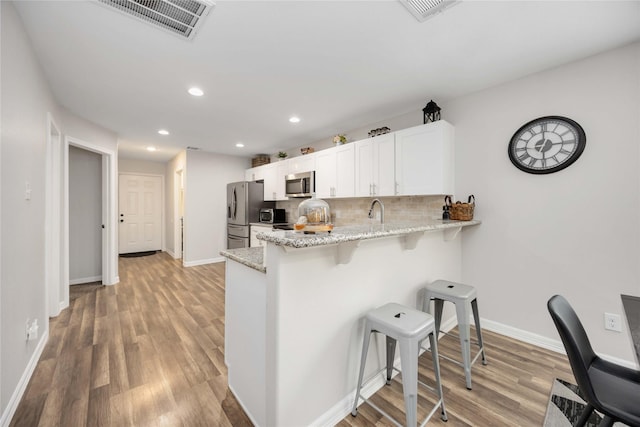 kitchen featuring kitchen peninsula, stainless steel appliances, a breakfast bar, backsplash, and white cabinets