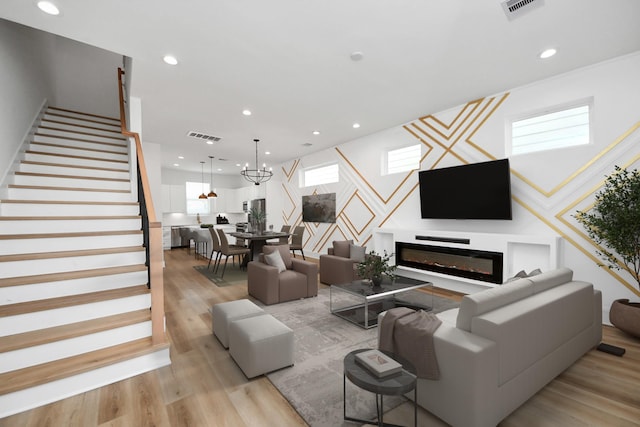 living room with recessed lighting, visible vents, light wood-style flooring, a glass covered fireplace, and stairs