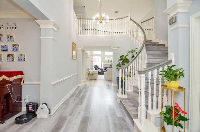 entrance foyer featuring ornate columns, wood-type flooring, a chandelier, a high ceiling, and ornamental molding