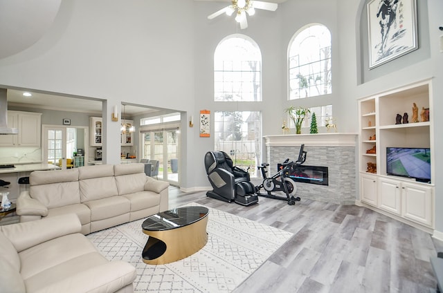 living room with built in shelves, light hardwood / wood-style floors, a towering ceiling, a tiled fireplace, and ceiling fan with notable chandelier