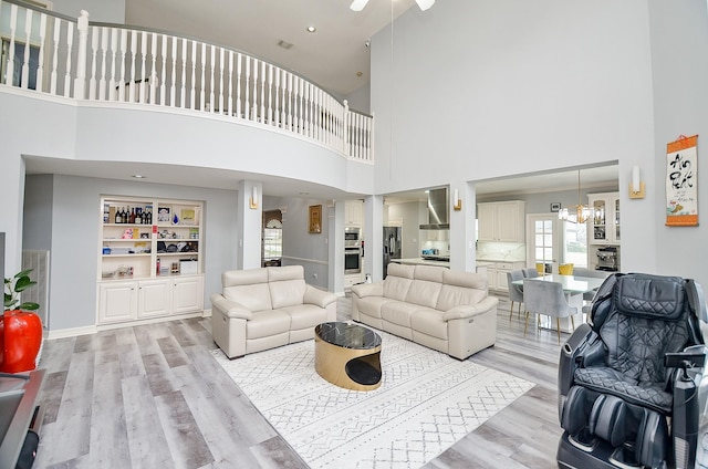 living room with built in shelves, a towering ceiling, a chandelier, and light hardwood / wood-style flooring