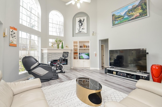 living room featuring built in shelves, light hardwood / wood-style floors, ceiling fan, and a towering ceiling