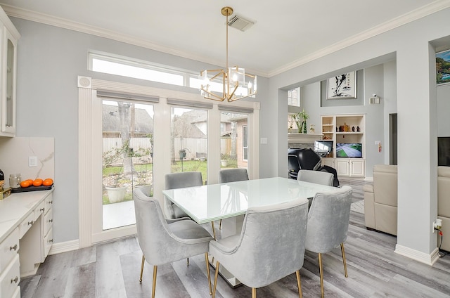 dining space featuring a fireplace, light hardwood / wood-style flooring, a notable chandelier, crown molding, and built in shelves