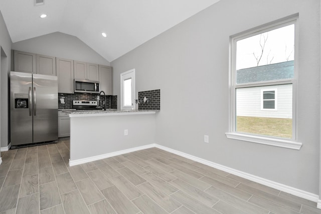 kitchen featuring gray cabinets, appliances with stainless steel finishes, backsplash, light stone countertops, and light hardwood / wood-style floors