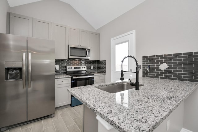 kitchen featuring sink, light stone countertops, kitchen peninsula, and appliances with stainless steel finishes