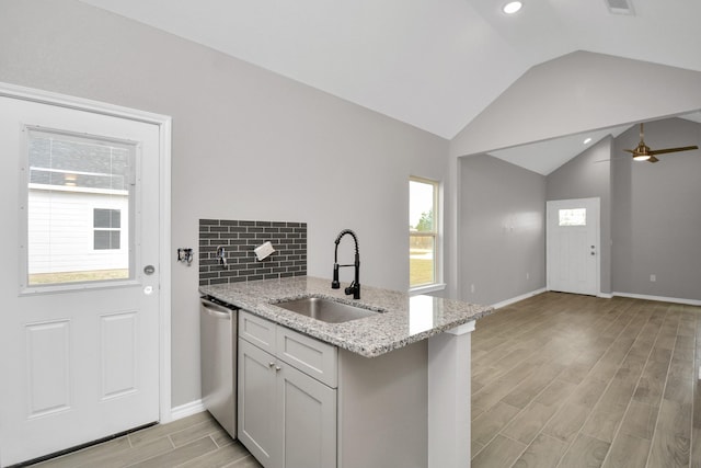 kitchen with dishwasher, sink, kitchen peninsula, light stone countertops, and light wood-type flooring