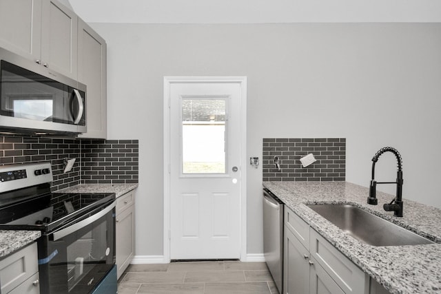 kitchen featuring appliances with stainless steel finishes, light stone countertops, sink, and backsplash