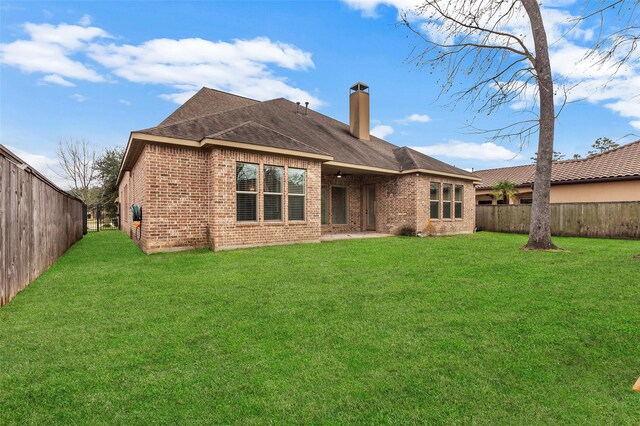 back of property featuring a lawn, a fenced backyard, a chimney, roof with shingles, and brick siding