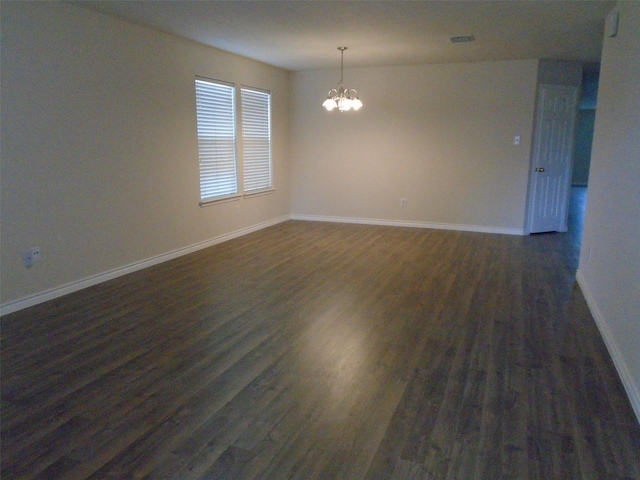 spare room featuring dark wood-type flooring and a notable chandelier