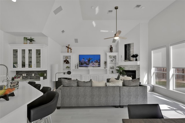 living room featuring ceiling fan, a stone fireplace, high vaulted ceiling, and light hardwood / wood-style flooring